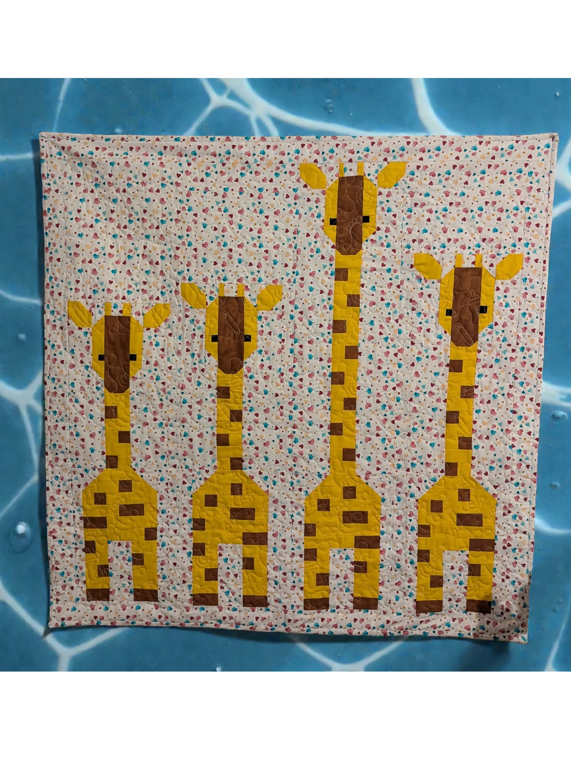 Babydecke mit Giraffenmotiv in Senfgelb und Braun auf gepunktetem Hintergrund, fotografiert auf Wasseroptik-Hintergrund.