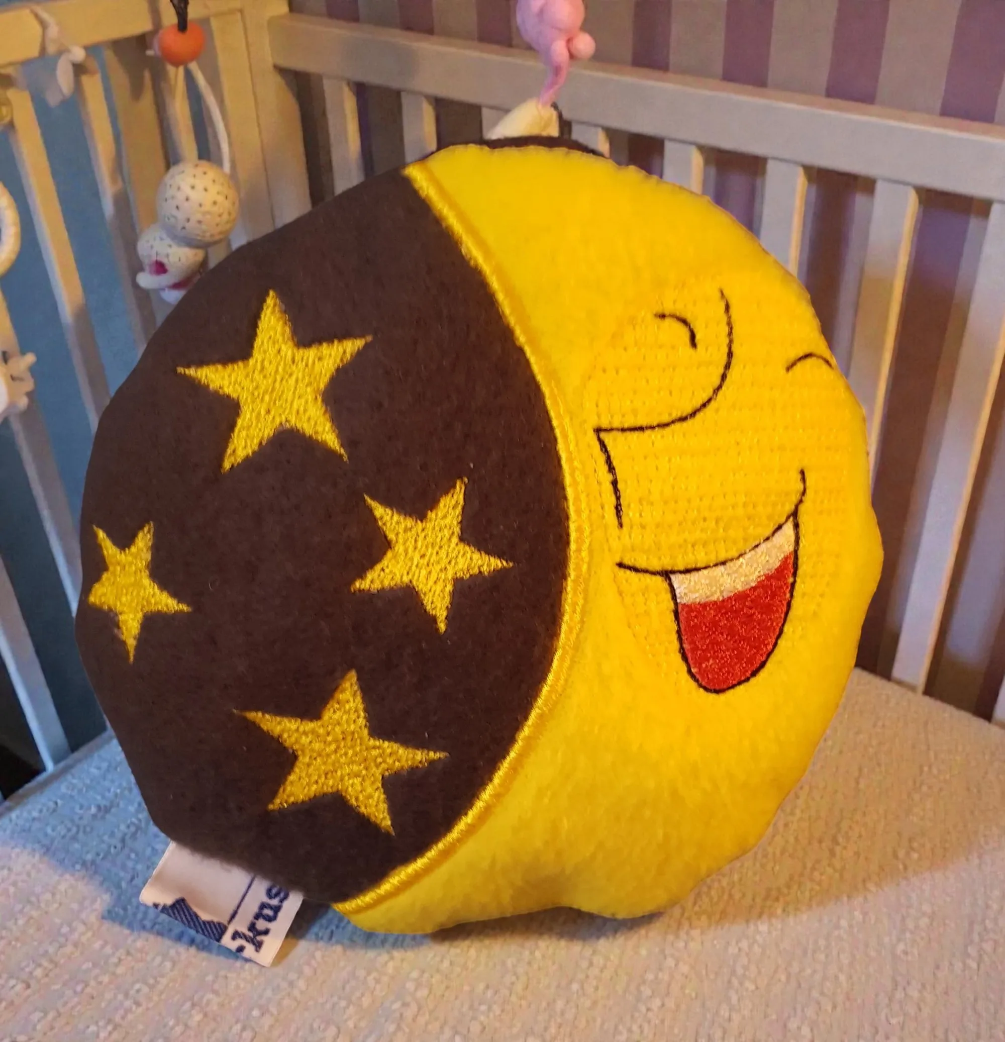 Kissen/Spieluhr 'Mond' mit gesticktem Gesicht und Sternen, aus gelbem und braunem Stoff im Kinderzimmer.