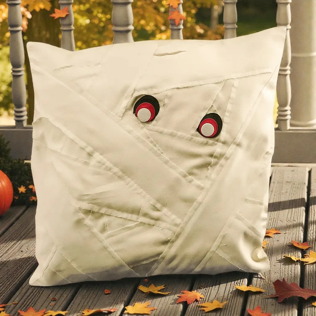 Kissen aus cremefarbenem Stoff mit schwarzen und roten Augen, umgeben von Herbstlaub auf einer Veranda.