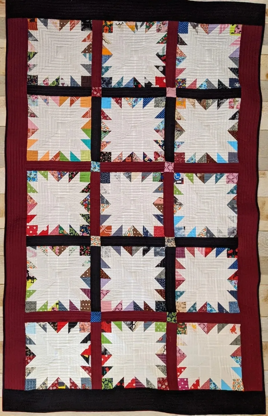 Quilt 'Bear Paw' mit geometrischen Mustern in Rot und Weiß, bunten Akzenten, auf Holzoberfläche.