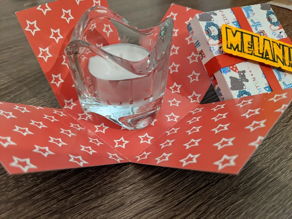 Explosionsbox aus rotem Papier mit weißen Sternen, Glasbehälter in der Mitte, personalisierte Dekoration mit Namen Melanie.