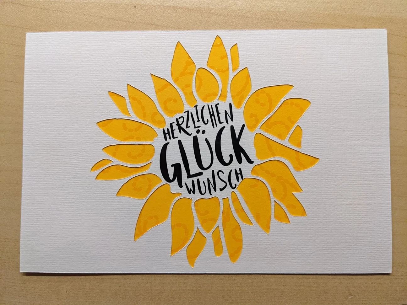 Glückwunschkarte mit gelber Sonnenblume und Schriftzug 'Herzlichen Glückwunsch' auf weißem Karton.