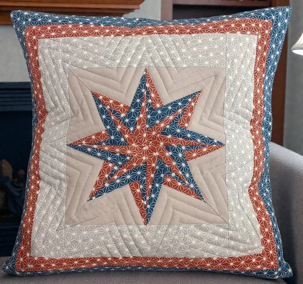 Kissen aus Baumwolle mit geometrischem Muster in Beige, Rostrot und Blau auf einem grauen Polstersessel.